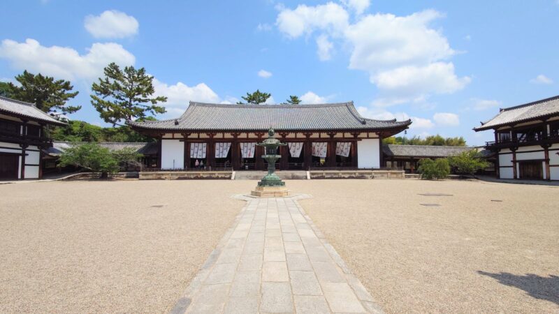 石畳の先に立つ金銅灯籠と、その奥に佇む法隆寺の大講堂の正面全景